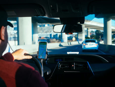 Driver uses a phone map in a car under a freeway overpass, following a blue car; map shows Cesar Chavez and AT&T Park.
