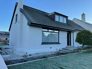 A modern white two-story house with a dark roof, large front window, and manicured lawn