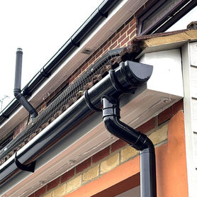 Close up looking up at new black plastic roofline downpipes and guttering fixed against light grey cladding