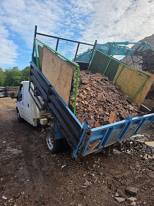 A truck with a tilted bed filled with rubble and debris unloads at a construction site