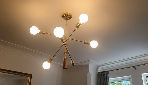 A modern, brass chandelier with five glowing bulbs extends from the ceiling