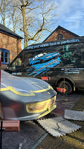 Black mobile car repair van with branded company graphics parked beside a car undergoing bodywork repairs