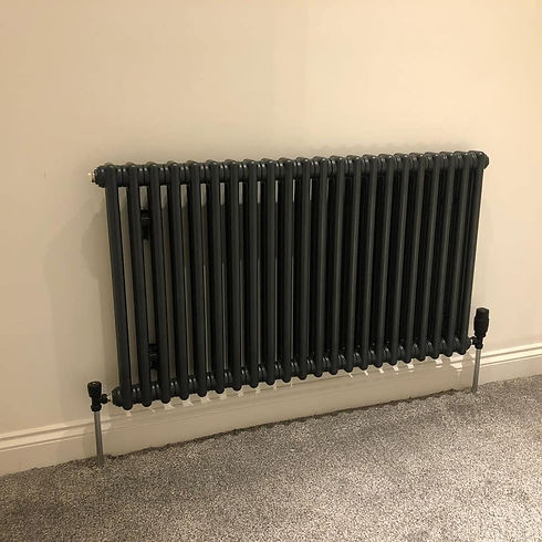 Modern black column radiator fitted on a light wall above grey carpet