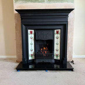 A black ornate fireplace with decorative white tiles featuring red floral patterns
