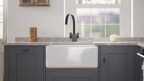 Close-up of a classic white ceramic Belfast sink set into dark grey shaker cabinetry with a modern matte black tap and light marble effect worktops.