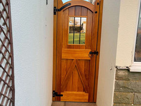 Bespoke arched wooden garden gate with a small latticed window pane set between house walls