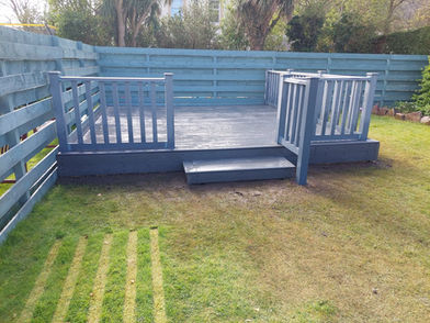 Painted grey timber decking area with steps and matching railings looking over a green grass lawn