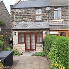 Stone cottage exterior with a small extension and skylights, surrounded by lush greenery and flowers