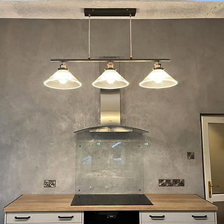 Modern dining area featuring three sleek glass pendant lights illuminating a smooth grey plaster wall finish