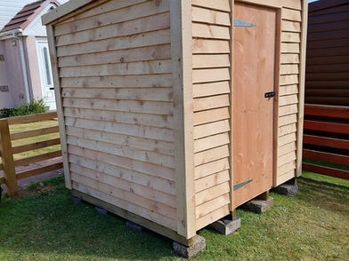 Small apex wooden garden shed with a single timber door standing on a green grass lawn
