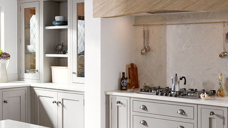 Shaker kitchen units under a wooden mantle beam with herringbone tiled splashback.