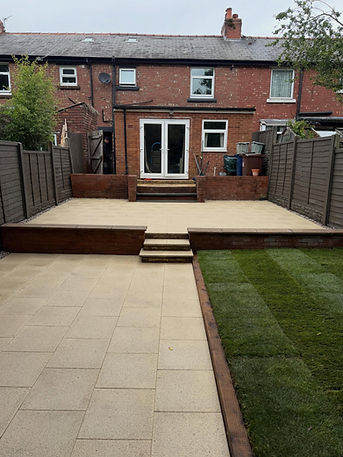 Elevated patio terrace featuring sandstone paving slabs, steps and retaining wall leading down to a lawn