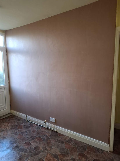 Internal wall surface split horizontally showing freshly applied pink skimming plaster drying evenly