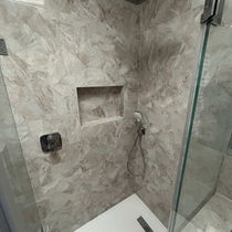 Modern shower with glass door, featuring beige marbled tiles, a built-in shelf, and a sleek showerhead