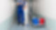 A person in blue overalls mops a narrow hallway. A cleaning cart with red and blue buckets is nearby