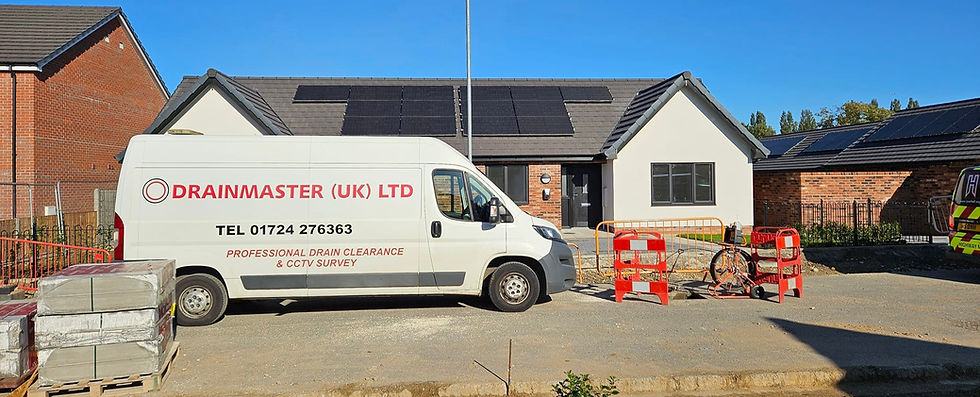 A white van with "DRAINMASTER (UK) LTD" written on it parked outside a residential building that has solar panels on the roof