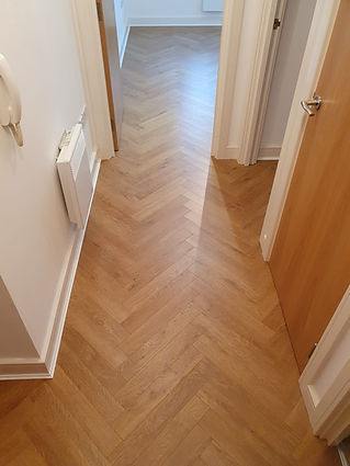 Narrow hallway with light wooden herringbone parquet flooring, white walls, and open wooden doors