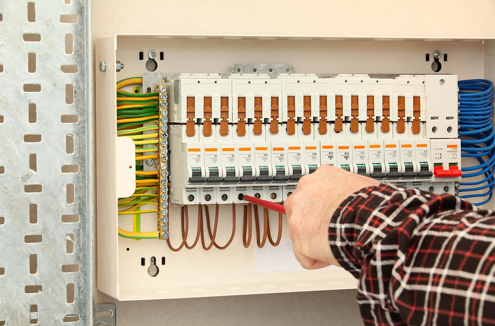 A person in a plaid shirt uses a screwdriver on a circuit breaker panel filled with colorful wires
