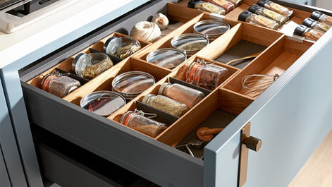 Open kitchen drawer with a wooden divider organizing various small spice jars.