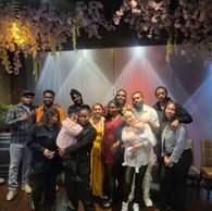 A large group of friends and family poses together for a photo under floral decorations