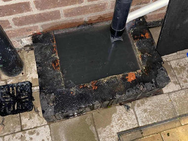 Black plastic gully trap against a brick wall filled to the brim with dirty standing water