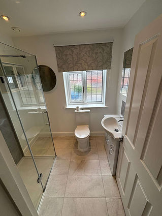 Small, bright bathroom with a glass shower, white toilet, and sink.