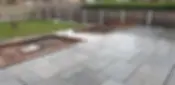Wet stone patio with large rectangular tiles, adjacent to a grassy lawn
