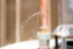 Close-up of a copper pipe with a water leak, spraying droplets.