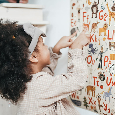 A child with curly hair and a headband points at letters on an alphabet poster featuring colourful animals