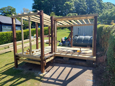 Wooden garden timber gazebo structure under construction with an open wooden frame on paving