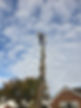 Arborist working at the top of a tall stripped tree trunk against a cloudy sky
