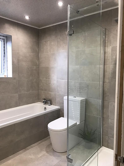 Modern bathroom with grey tiles, featuring a white bathtub, toilet, and glass-enclosed shower