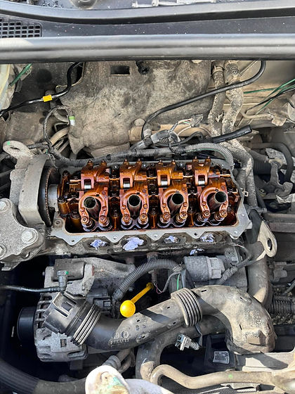 Open camshaft area of a car engine showing rocker arms bathed in gold motor oil inside the cylinder head