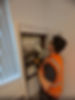 A technician in an orange vest examines an electrical panel in a brightly lit room