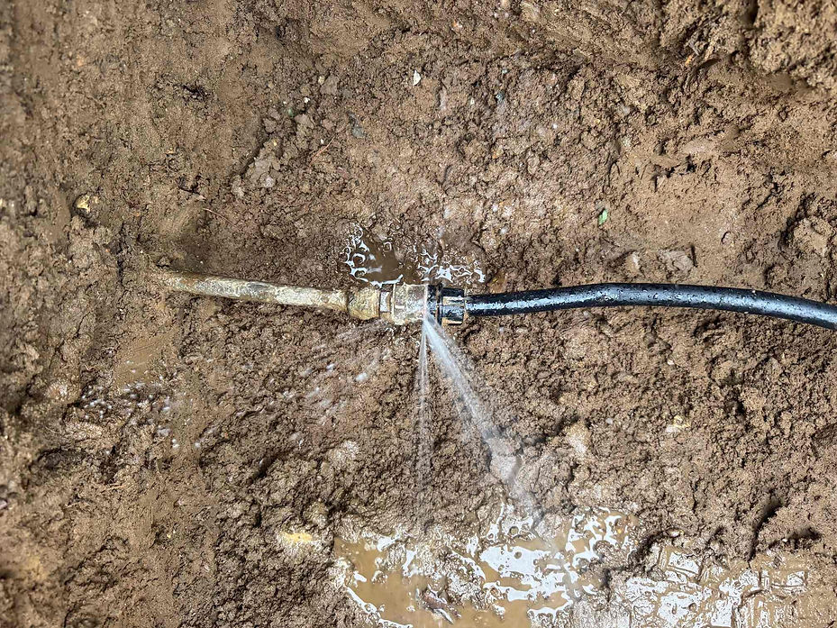 Alt text: A high-angle view of an underground water pipe joint leaking water into the surrounding muddy brown earth.
