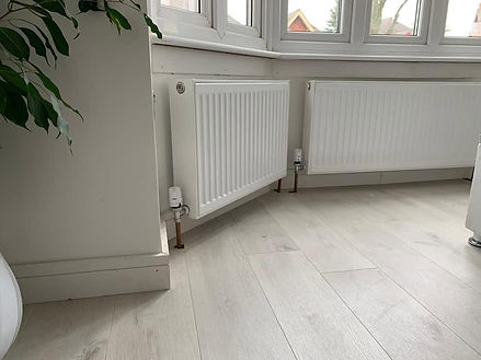 Two white panel radiators installed in a bright room with light laminate flooring