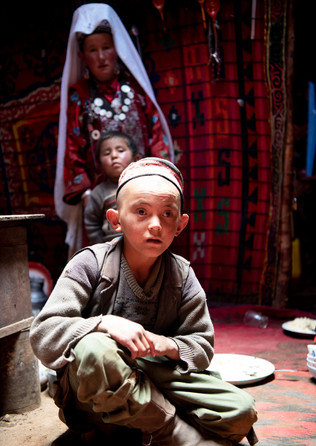 The light from the opening of the roof of the yurt shines onto a young Kyrgyz boy's face. His mother and brother stand behind him.
- Wakhan Corridor, Afghanistan.