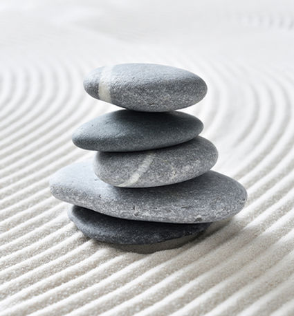 Stacked smooth stones on raked sand, representing balance and harmony.