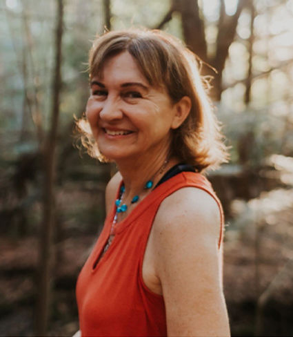 Brigitta Sebesta, owner of sebesta somatics LLC in red tank top and necklace in a forest background.