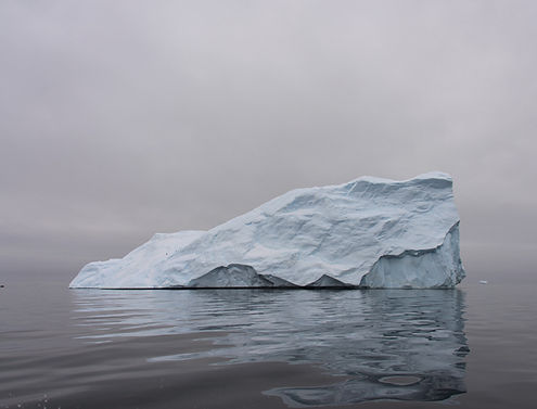 Large iceberg floating in the water, cloudy sky background, scenic view.