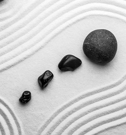 Four black stones arranged on white sand with wave patterns background.