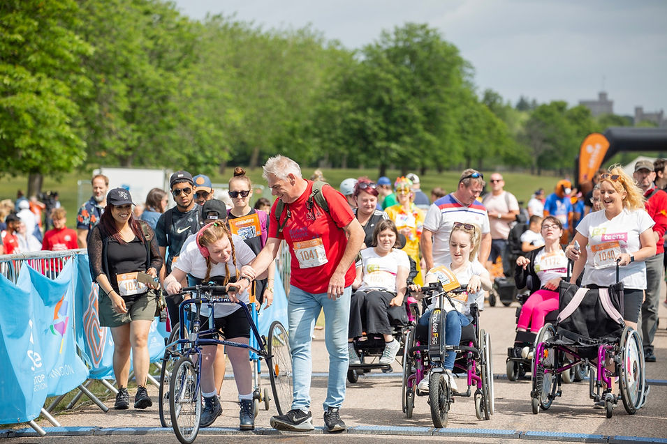 A group of youngsters in wheelchairs and one on a frame runner participating in a mass fundraising walk for CP Teens UK.