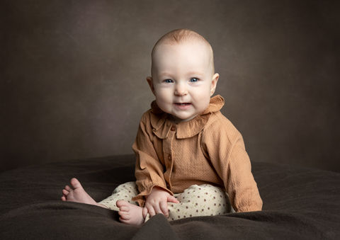 Babyfotografering af pige siddende med brun baggrund