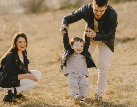 Padre jugando con su hijo mientras la madre observa sonriente, representando momentos de unión y felicidad familiar.