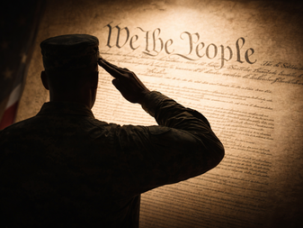 Silhouette of a military veteran saluting an illuminated copy of the United States Constitution.