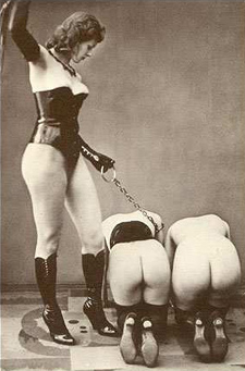 Dominatrix in latex corset holding chain attached to two submissives.