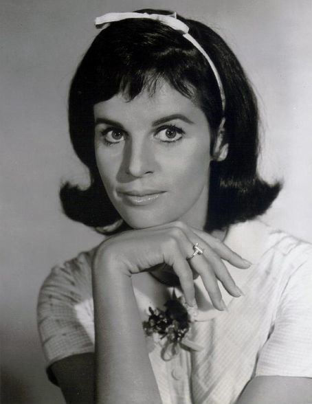 Dark-haired woman with headband, chin resting on hand, wearing ring, white shirt.