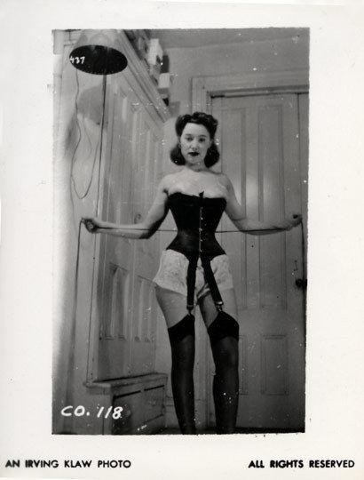 Pin-up woman in corset and stockings, CO. 118, standing indoors.