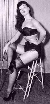 Woman in lingerie, stockings, garter belt, seated, holding a whip.