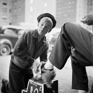 Young boy kneels, shining a customer's shoe on a city street.